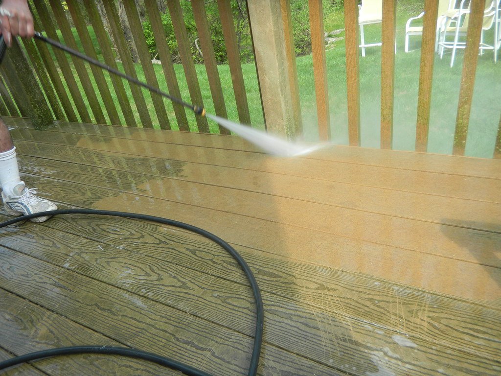Pressure washer wand cleaning a wooden deck, clean stripe next to weathered boards