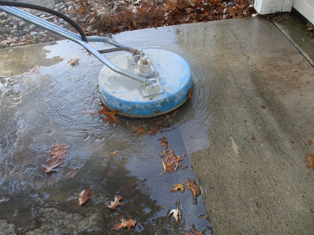 Surface cleaner lifting grime off a concrete driveway, leaving a clean path